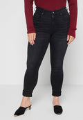 Schwarze, enge Jeans mit hoher Taille, Fronttaschen und einer leicht abgenutzten Textur. Kombiniert mit einem kastanienbraunen, gerippten Oberteil und schwarzen Pantoletten.