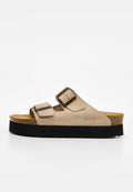 Beige Velours-Slidesandale mit zwei verstellbaren Schnallen, Kork-Fußbett, schwarzer Plateau-Sohle und Bayton-Logo an der Seite.