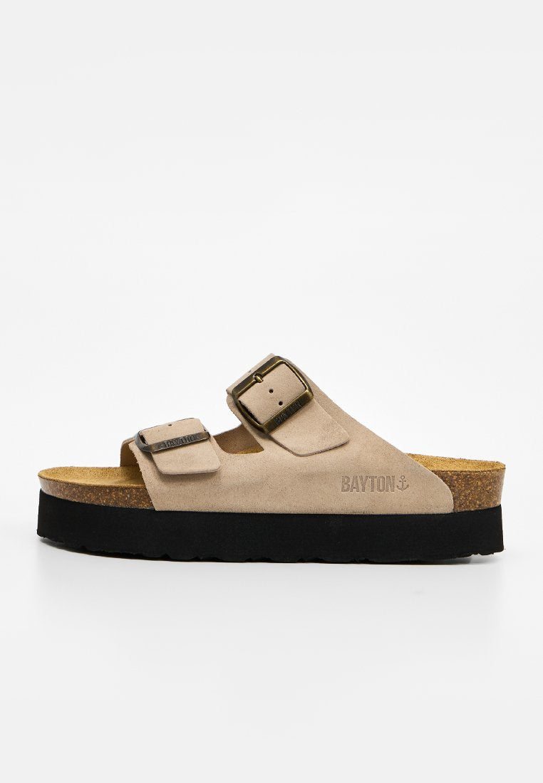 Beige Velours-Slidesandale mit zwei verstellbaren Schnallen, Kork-Fußbett, schwarzer Plateau-Sohle und Bayton-Logo an der Seite.