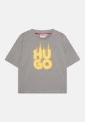 Graues T-Shirt mit kurzen Ärmeln, das einen großen, gelben grafischen Textdruck mit "HU GO" im Used-Look zeigt. Aus Baumwollmaterial mit Rundhalsausschnitt.
