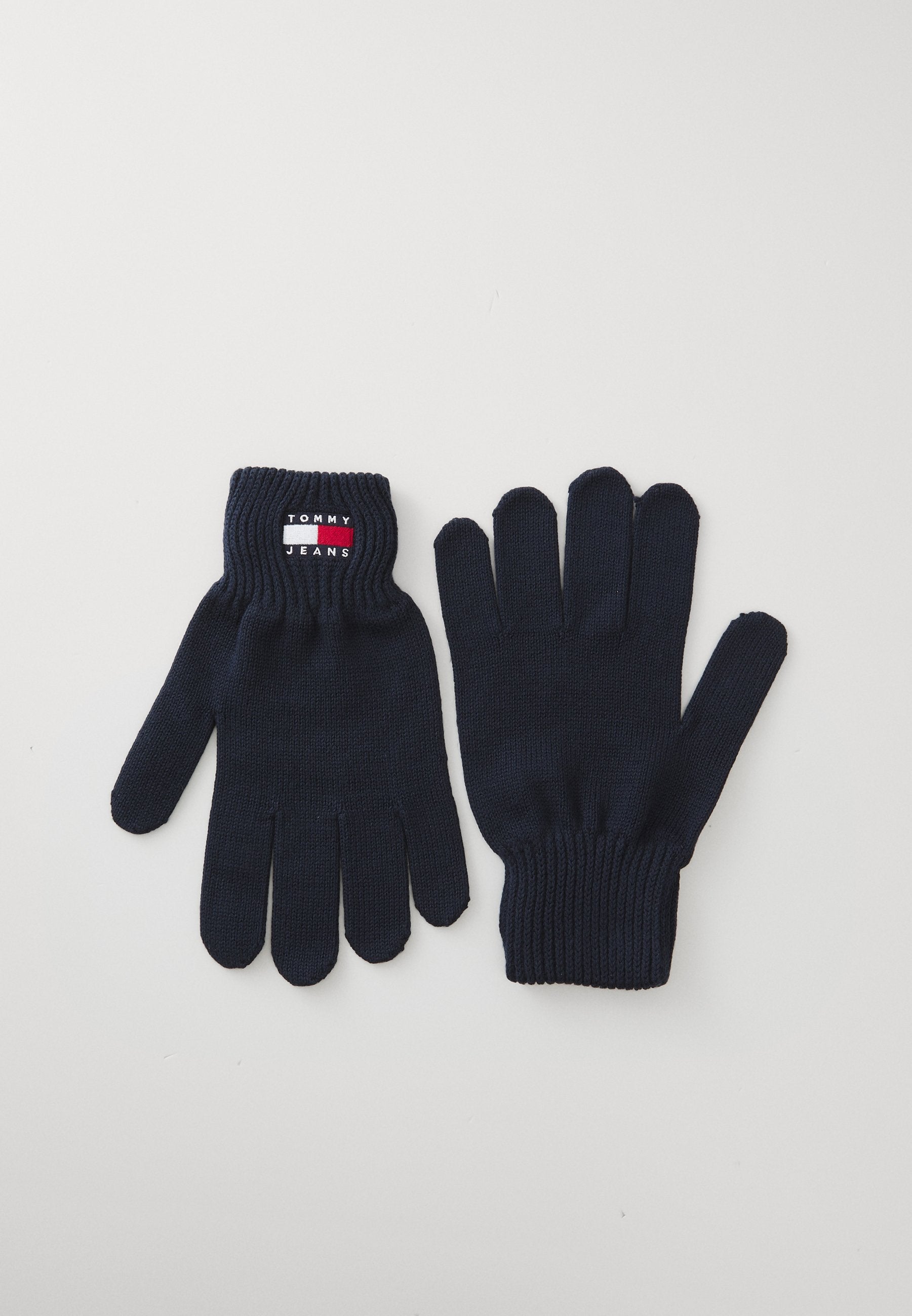 Marineblaue gestrickte Handschuhe mit geripptem Bündchen, ausgestattet mit einem kleinen Markenetikett in Rot- und Weißtönen. Fünf-Finger-Design für Geschicklichkeit.
