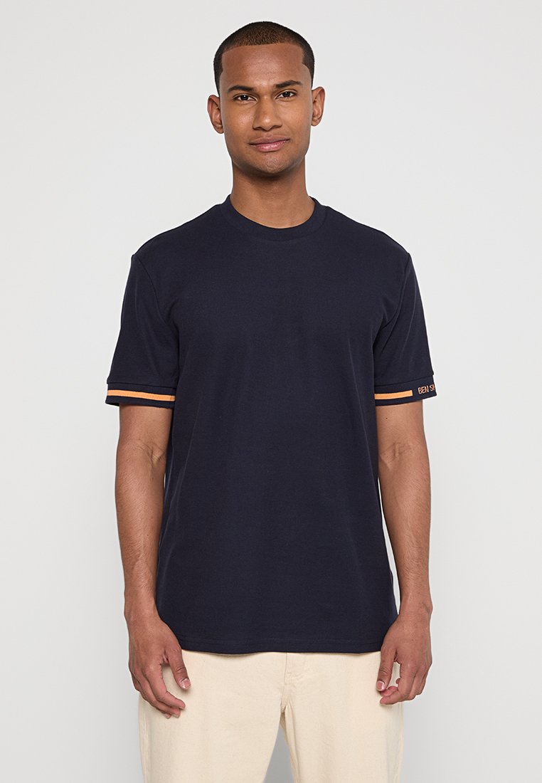 Kornblumenblaues T-Shirt mit kurzen Ärmeln aus Baumwolle, mit orangefarbenen Streifenakzenten an den Ärmeln und einem runden Ausschnitt.