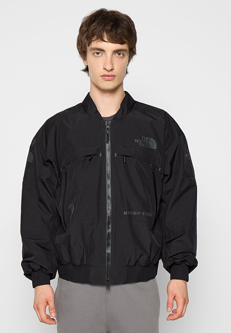 Schwarze Zip-Jacke aus leichtem Material, mit einem elastischen Taillenbund, großen Taschen und Logostickereien auf der Brust und den Ärmeln.