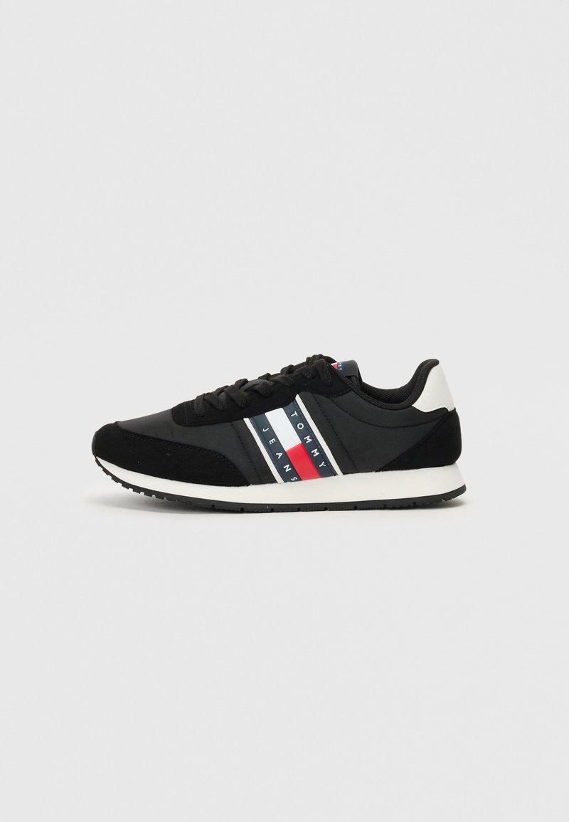 Schwarzer Sneaker mit strukturiertem Stoff und Wildleder-Akzenten. Verfügt über eine weiße Zwischensohle und drei horizontale Streifen in Rot, Weiß und Blau.