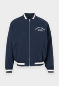 Marineblaue Bomberjacke mit Reißverschluss, weißen gestreiften Bündchen und Saum, mit der Aufschrift "Tommy Jeans Since 1985 New York City" auf der linken Brust.