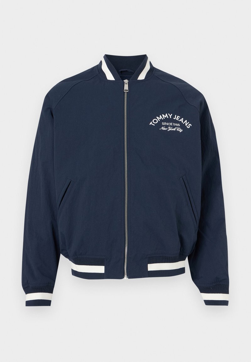 Marineblaue Bomberjacke mit Reißverschluss, weißen gestreiften Bündchen und Saum, mit der Aufschrift "Tommy Jeans Since 1985 New York City" auf der linken Brust.