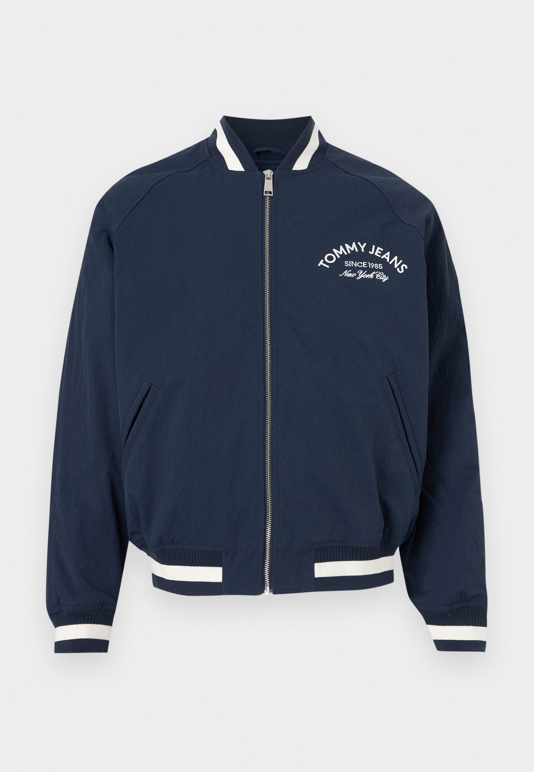 Marineblaue Bomberjacke mit Reißverschluss, weißen gestreiften Bündchen und Saum, mit der Aufschrift "Tommy Jeans Since 1985 New York City" auf der linken Brust.