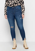 Schlanke Jeans aus mittelblauem Denim mit ausgefransten Knien und geschnittenen Säumen. Kombiniert mit einer blauen und beigen gemusterten Bluse und cremefarbenen Stiefeletten.