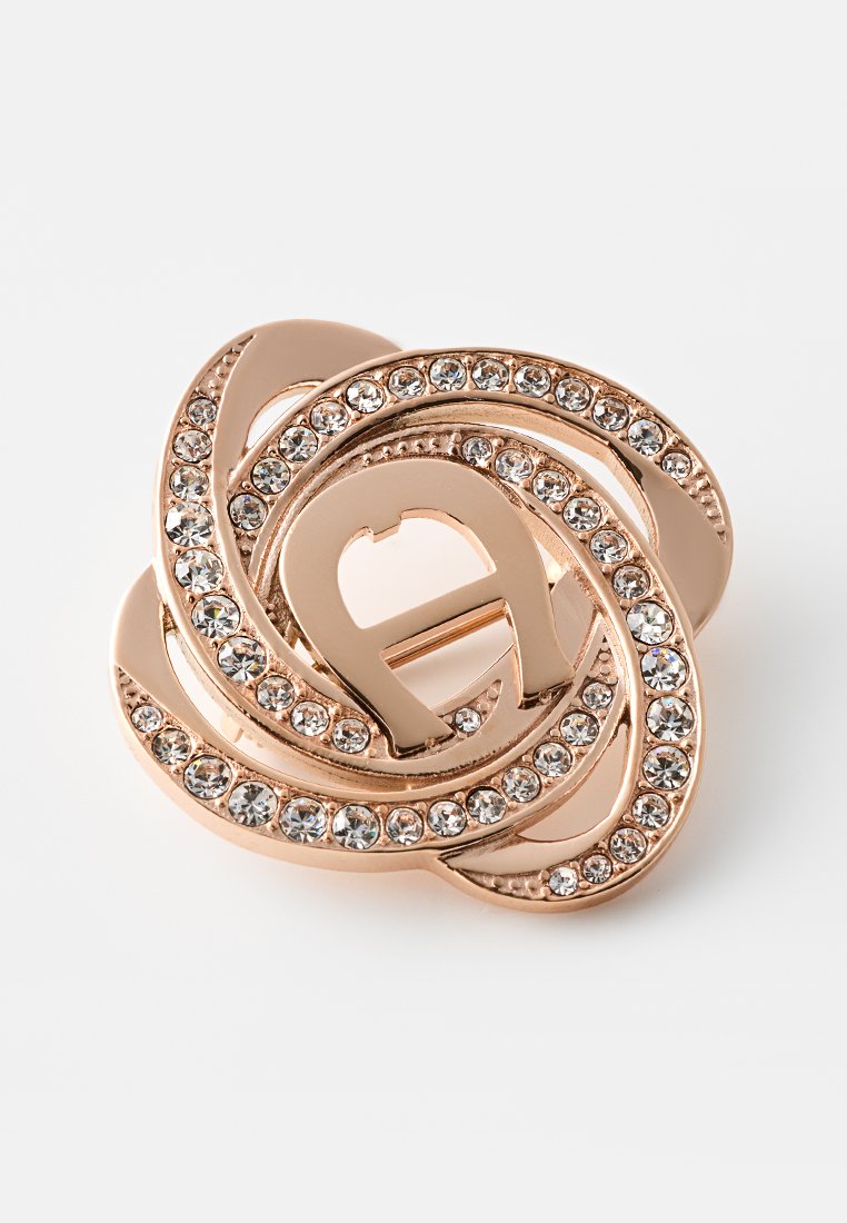 Rosegold-Brosche mit ineinander verschlungenen Schlaufen, verziert mit klaren Strasssteinen, die ein funkelndes Floraldesign auf weißem Hintergrund erzeugen.
