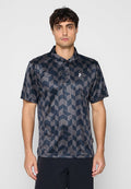 Mann trägt ein kurzärmeliges Poloshirt mit einem schwarz-grauen geometrischen Würfelmuster und steht vor einem einfarbigen hellen Hintergrund.