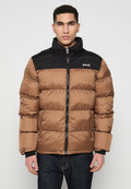 Mann, der eine braune und schwarze gepolsterte Jacke mit Reißverschlusstaschen trägt und vor einem schlichten hellen Hintergrund steht.