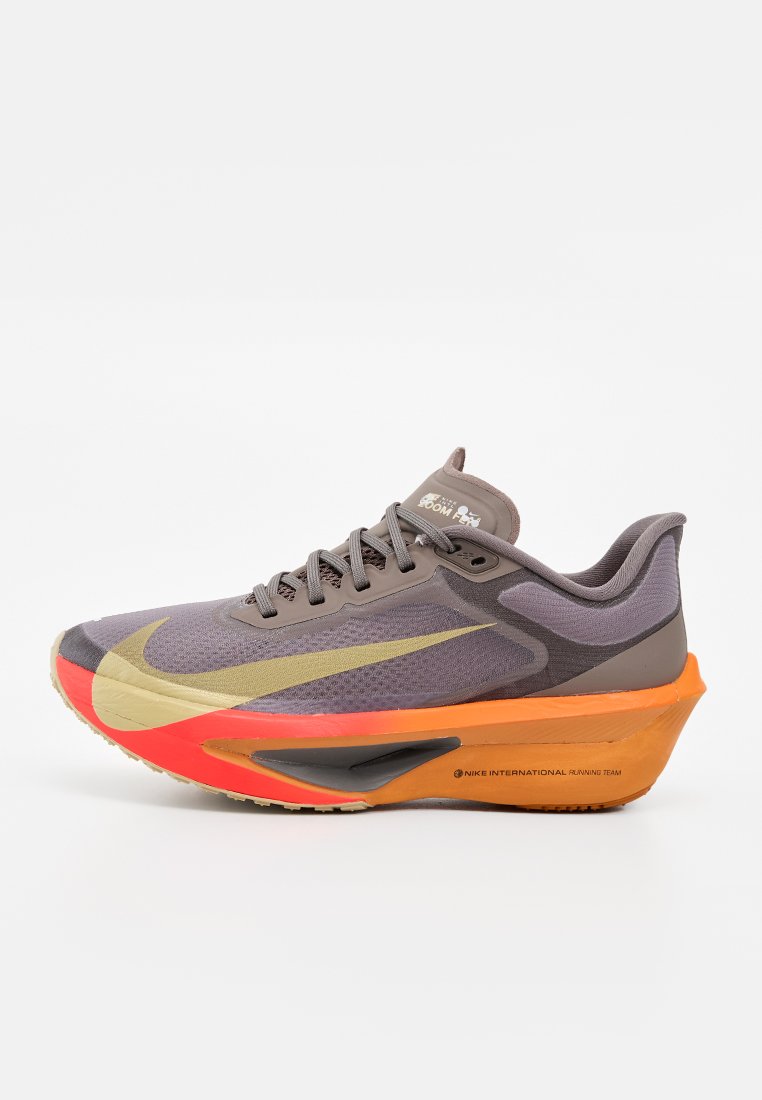 Grau-orangefarbener Nike Laufschuh mit großem gelbem Swoosh und dicker Sohle, von der Seite auf weißem Hintergrund gesehen.