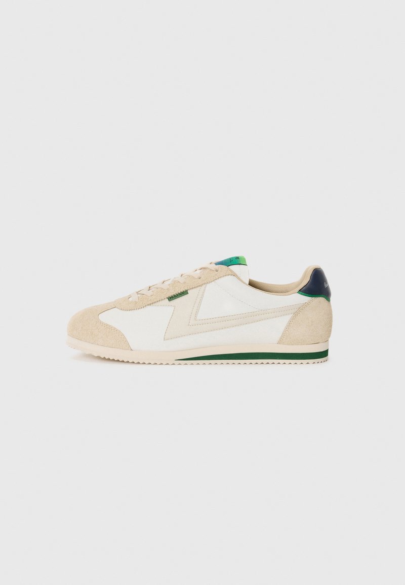 Sneaker mit einem Obermaterial aus weißem Stoff, beigen Wildlederelementen, einem grünen Fersenpatch und einer strukturierten Gummisohle im klassischen Low-Top-Design.