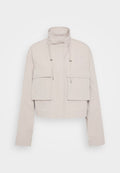 Gekürzte beige Jacke aus leichtem Stoff. Verfügt über einen hohen Kragen, zwei aufgesetzte Taschen vorne und verstellbare Kordeln am Hals.