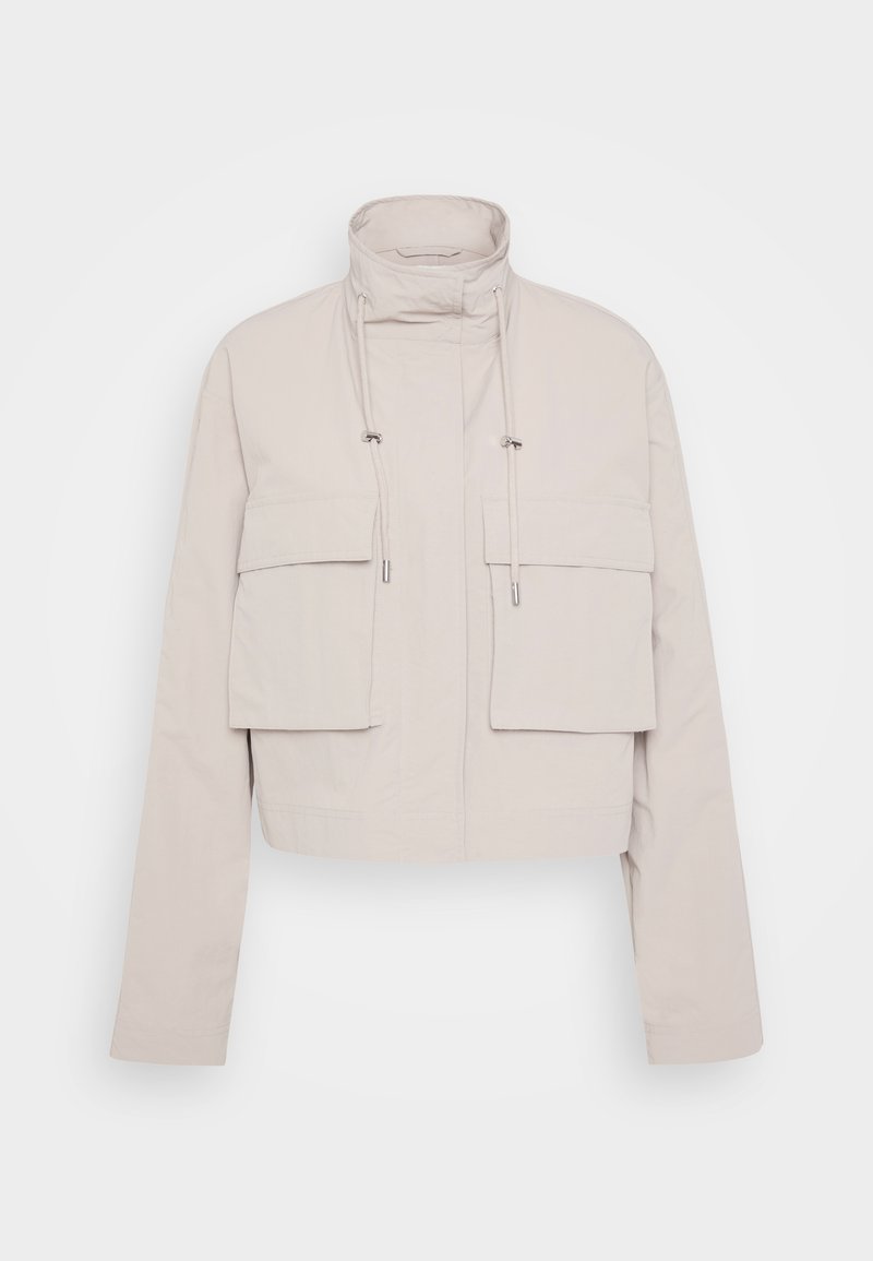 Gekürzte beige Jacke aus leichtem Stoff. Verfügt über einen hohen Kragen, zwei aufgesetzte Taschen vorne und verstellbare Kordeln am Hals.