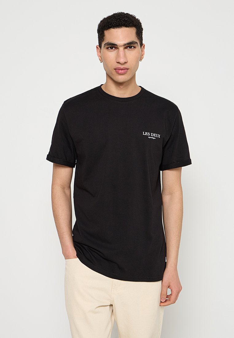 Schwarzes Baumwoll-T-Shirt mit umgeschlagenen Ärmeln, ausgestattet mit einem weißen "LES DEUX"-Logo auf der linken Brust. Klassischer Rundhalsausschnitt und lockere Passform.