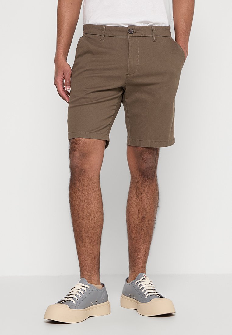 Braune Baumwollshorts mit geradem Schnitt, fünf Taschen und Knopfverschluss, kombiniert mit grauen Sneakers und einem weißen Rundhalsausschnitt-T-Shirt.