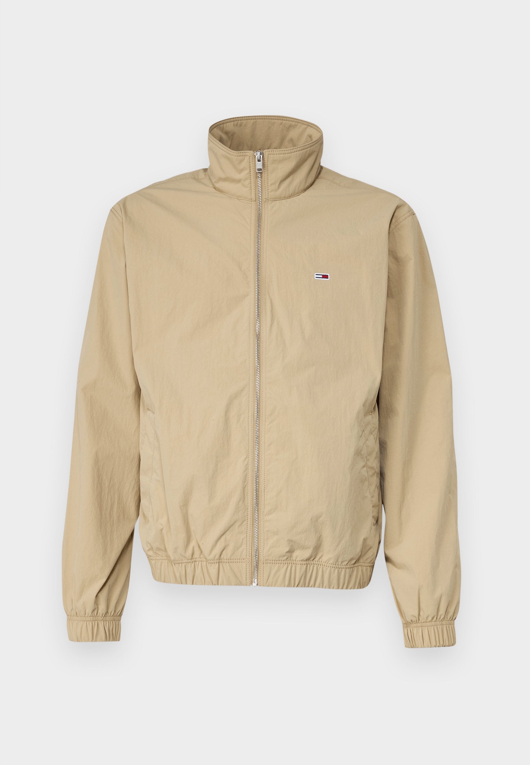 Beige leichte Jacke mit hohem Kragen, Reißverschluss, elastischen Bündchen und Saum, mit kleinem Logo auf der linken Brust. Glatte Textur.