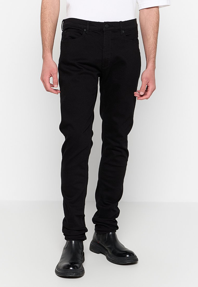 Schwarze Jeans aus Denim mit schlanker Passform, ausgestattet mit fünf Taschen, einem Reißverschluss und feinen Nähdetails. Der Stoff hat eine glatte Textur.