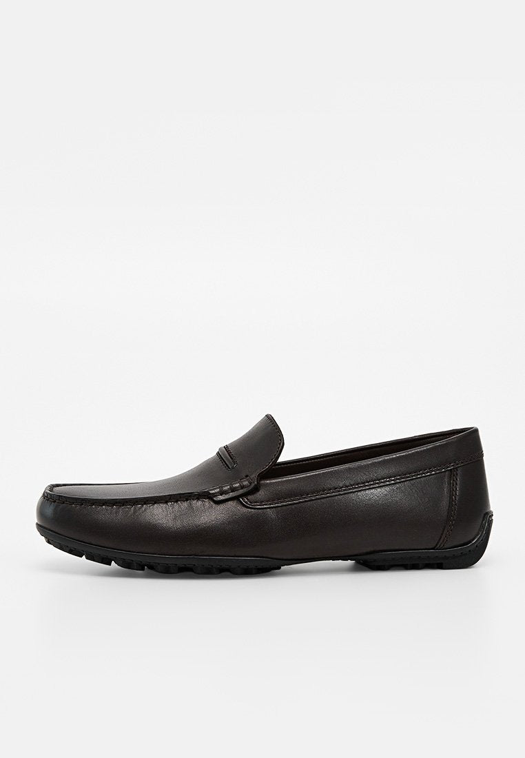 Schwarzer Leder-Slipper mit genähtem Obermaterial und strukturierter Gummisohle, seitlich auf weißem Hintergrund gezeigt.