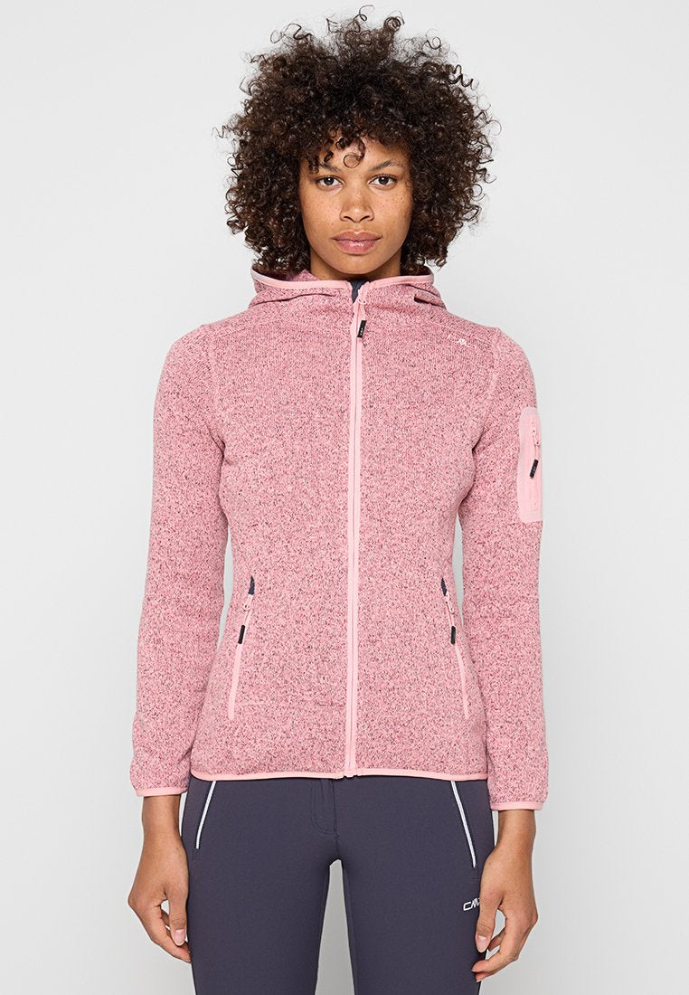 Frau mit lockigem Haar, die eine pinke Fleecejacke mit Reißverschluss, Kapuze und Reißverschlusstaschen trägt, steht vor einem einfarbigen Hintergrund.
