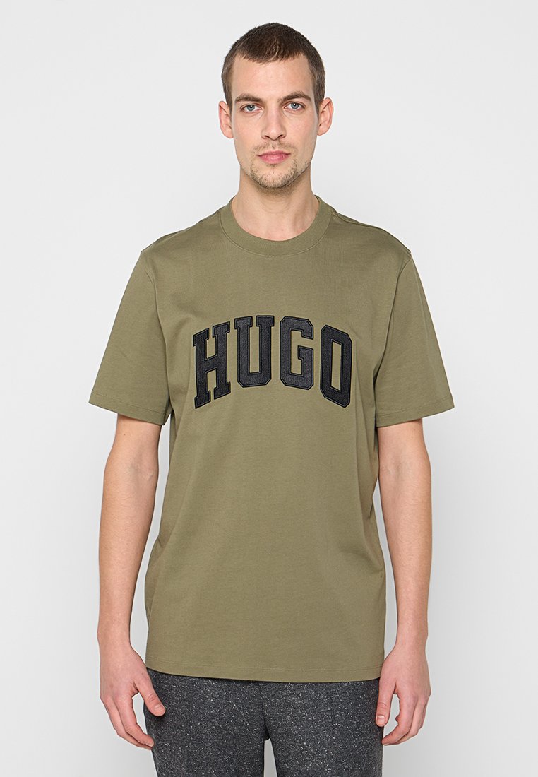 Olivgrünes Baumwoll-T-Shirt mit einem schwarzen, gestickten "HUGO"-Logo auf der Vorderseite. Kurze Ärmel und Rundhalsausschnitt. Reguläre Passform.