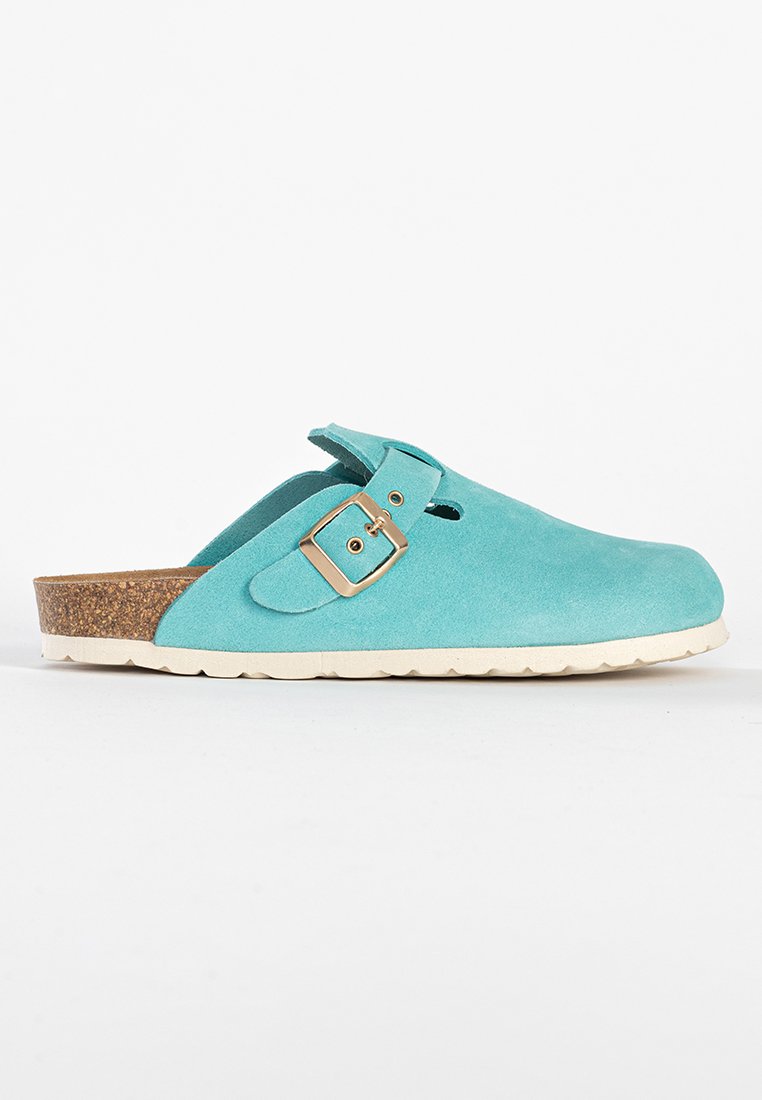 Hellblaue Wildleder-Schlupfschuhe mit verstellbarem Schnallenriemen, Korkfußbett und weißer gerippter Sohle, dargestellt im Seitenprofil.