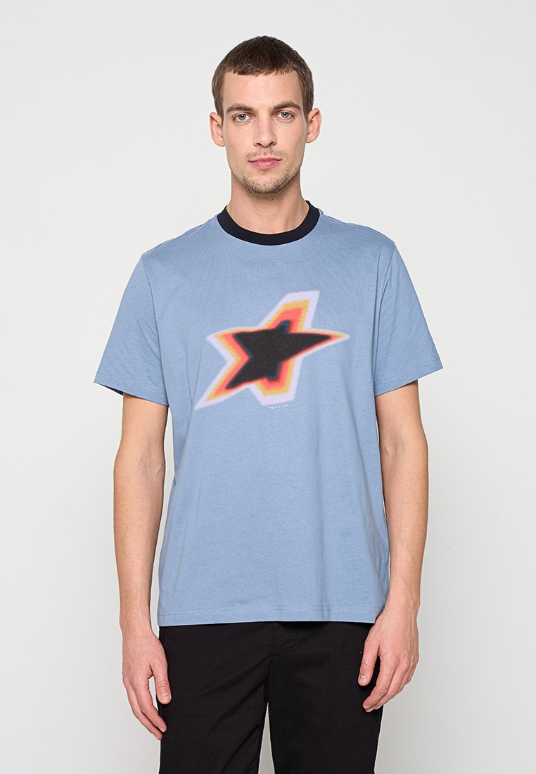 Hellblaues Baumwoll-T-Shirt mit einem schwarzen Stern in der Mitte, umgeben von einer roten und orangefarbenen Umrandung, und einem dunklen Kragen. Schlichtes Design mit kurzen Ärmeln.