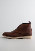 Braune Leder-Ankelstiefel mit glatter Oberfläche, ausgestattet mit goldenen Ösen, einer cremefarbenen Sohle und einer rot-blauen Akzent-Schlaufe an der Rückseite.