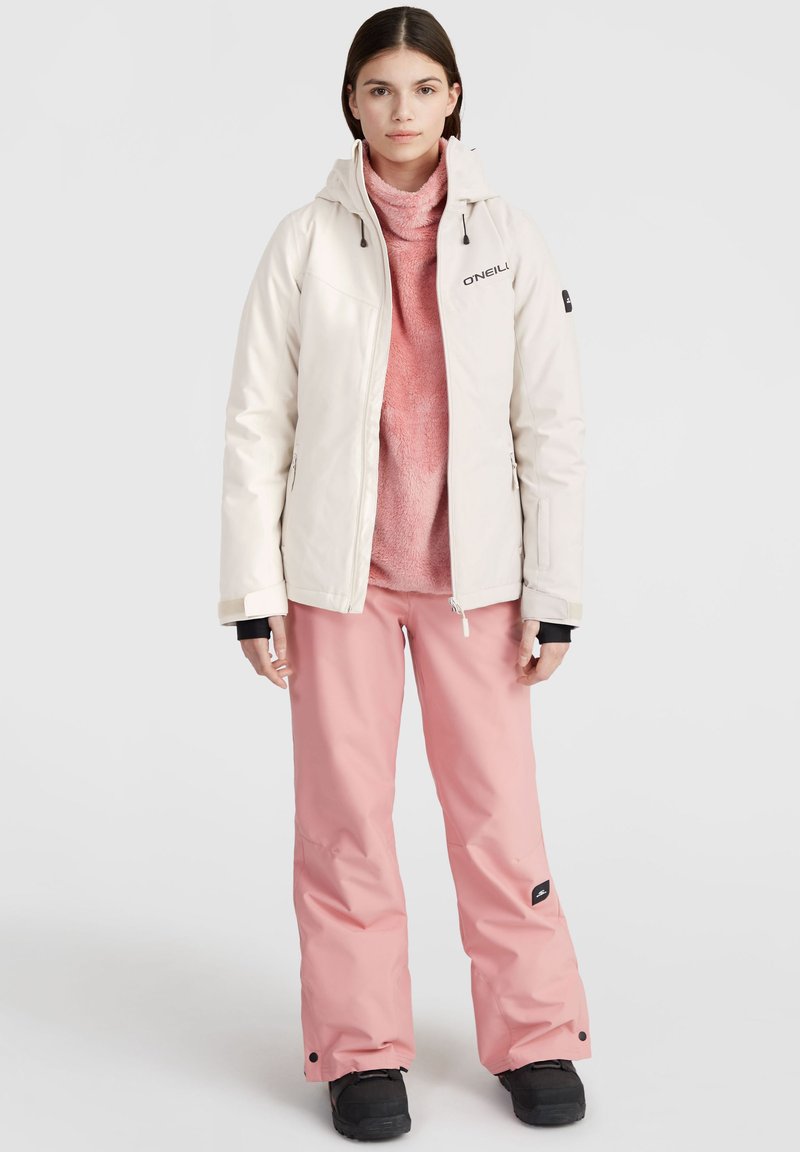 Hellbeige Jacke mit Kapuze, Reißverschluss; rosa Fleece-Pullover; rosa Schnee-Hose; schwarze Stiefel; minimales Branding auf der Jacke und den Hosen.