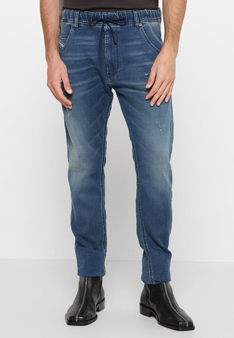 Helle blaue Denim-Jogger-Hosen mit einem elastischen Bund und Kordelzug. Mit vorderen Taschen und dezentem Used-Look. Getragen mit schwarzen Stiefeln.