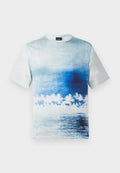 Kurzärmeliges T-Shirt mit blau-weißem Farbverlauf, der eine Strandszene mit Palmen und Wasserreflexionen zeigt.