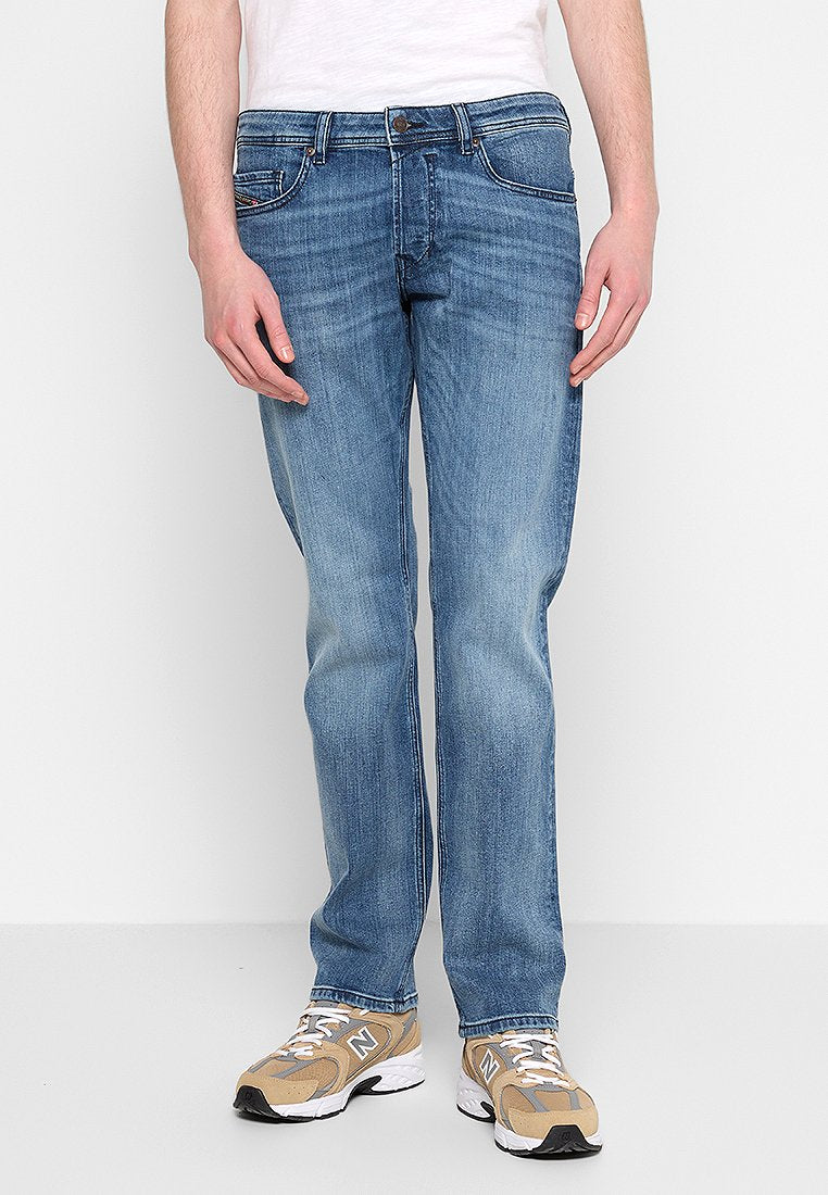 Hellblaue Jeans aus Denim mit geradem Schnitt, ausgestattet mit fünf Taschen, Gürtelschlaufen und subtiler Ausbleichung. Kombiniert mit beigen Sneakers.