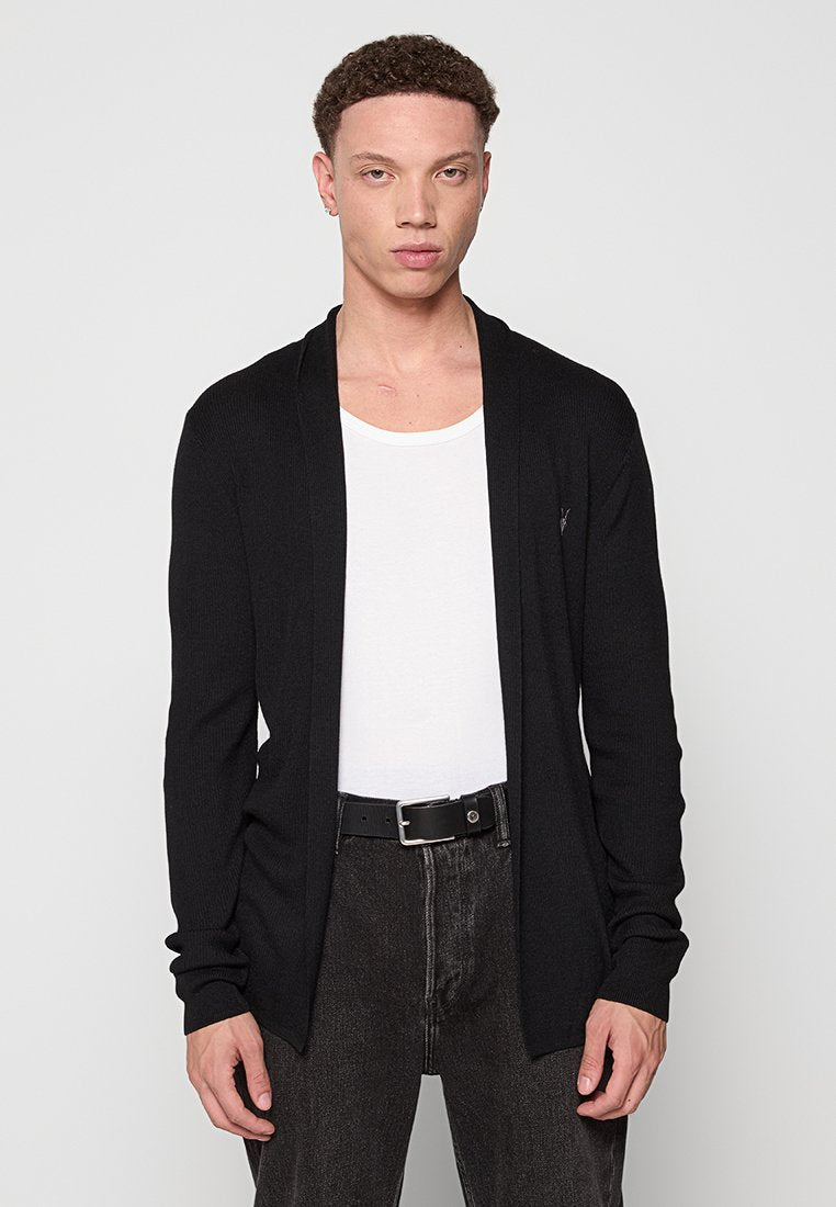 Schwarze Langarm-Cardigan aus geripptem Strick, mit offenem Vorderteil, kombiniert mit einem weißen Tanktop und dunklen Hosen. Minimalistischer Stil.