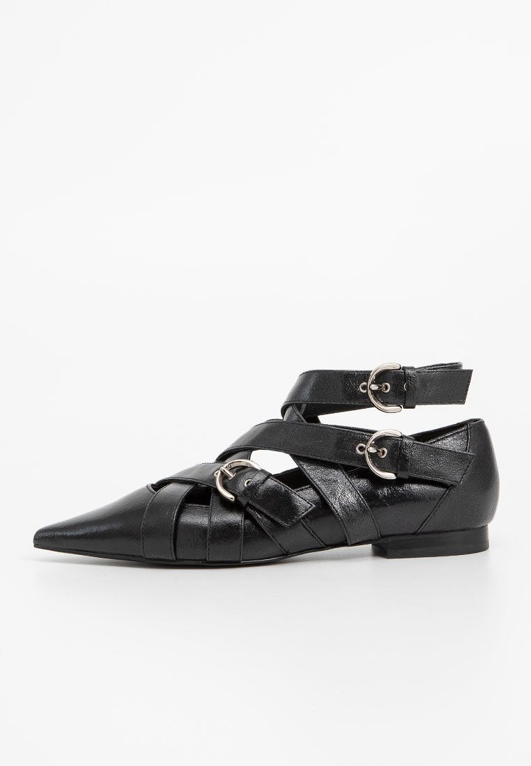 Schwarze flache Schuhe mit einer spitzen Zehe, aus glattem Leder. Sie verfügen über überkreuzte Riemen und silberne Schnallenakzente mit einem niedrigen Absatz.