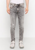 Helle graue, ausgefranste Jeans mit schmalem Schnitt, die mit Rissen und fransigen Akzenten versehen sind. Hergestellt aus Denim, ergänzt durch einen Gürtel und Sneakers.