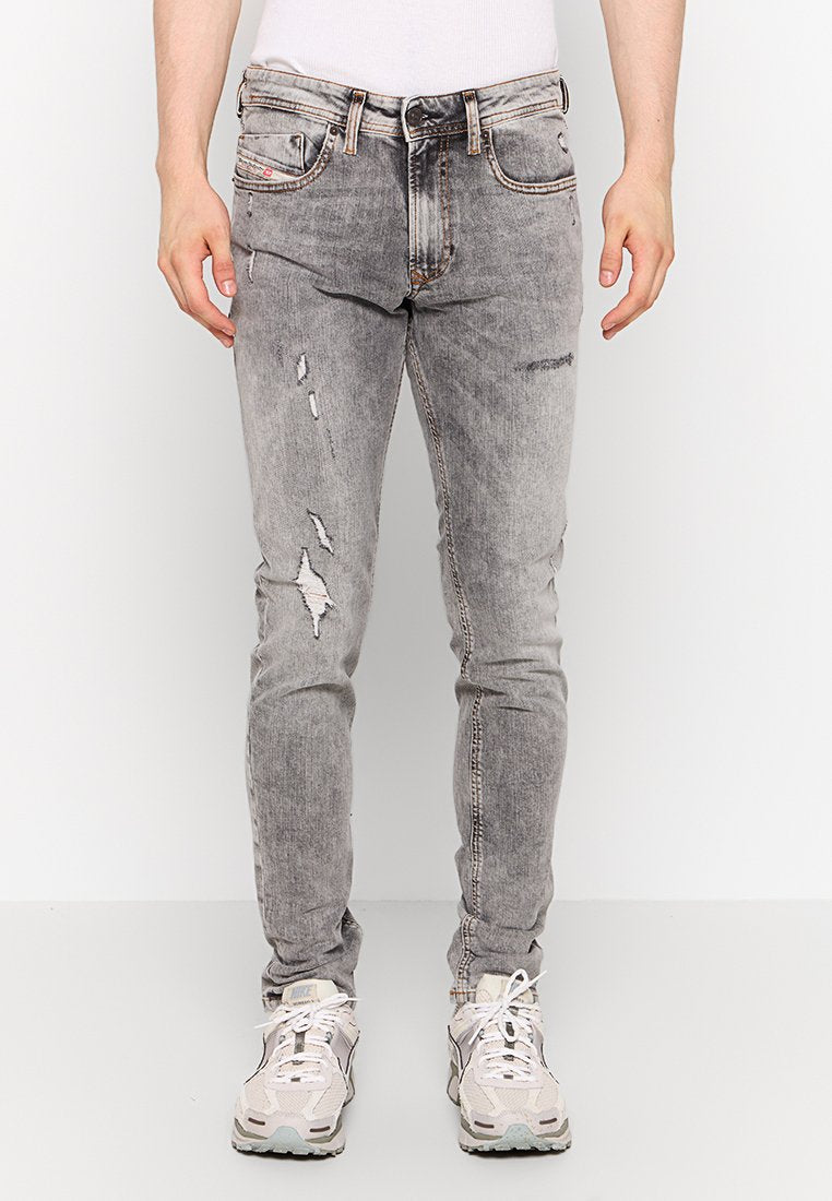 Helle graue, ausgefranste Jeans mit schmalem Schnitt, die mit Rissen und fransigen Akzenten versehen sind. Hergestellt aus Denim, ergänzt durch einen Gürtel und Sneakers.