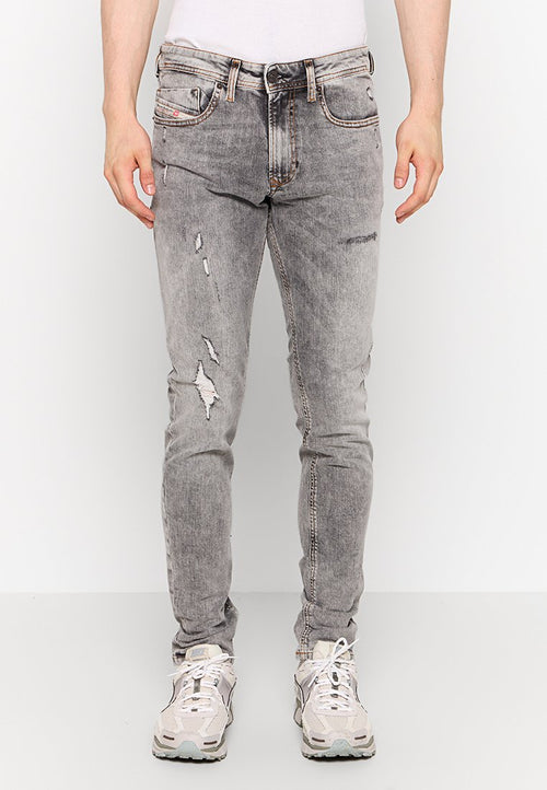 Helle graue, ausgefranste Jeans mit schmalem Schnitt, die mit Rissen und fransigen Akzenten versehen sind. Hergestellt aus Denim, ergänzt durch einen Gürtel und Sneakers.