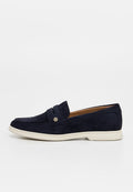 Marineblauer Wildleder-Loafer mit weißer Sohle, Pennyriemen mit kleinem rundem Metallemblem und gesteppten Details.