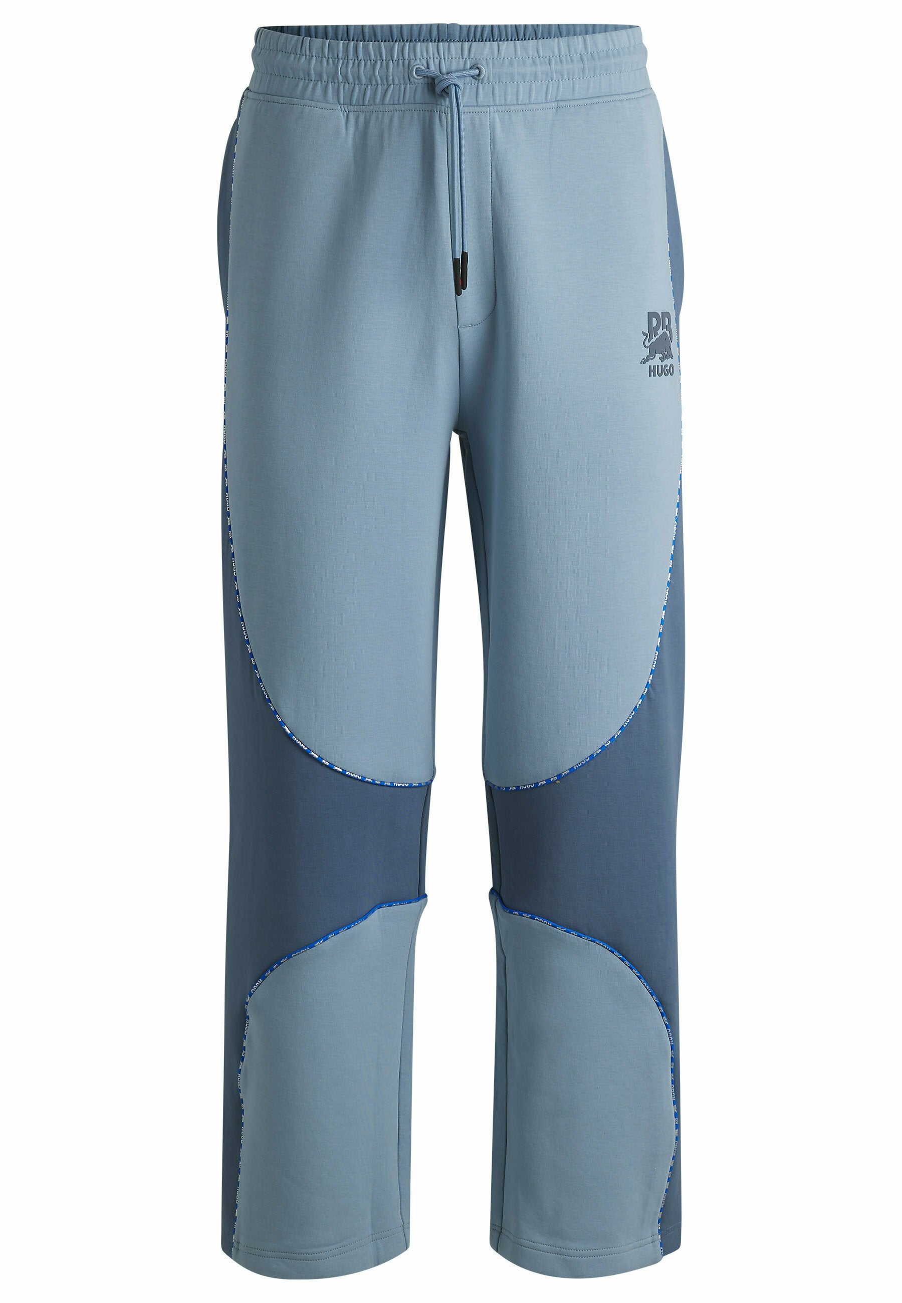 Hellblaue Sweatpants mit einer Mischung aus helleren und dunkleren blauen Stoffpaneelen, elastischem Bund mit Kordelzug und Kontrastnähten.