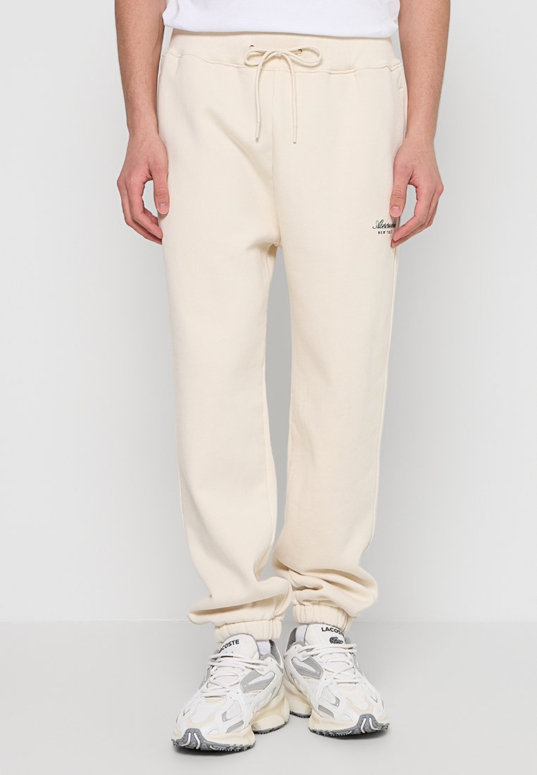 Beige Jogginghose mit elastischem Bund und Kordelzug, mit Bündchen an den Knöcheln, aus weichem Stoff und mit kleinem Markenlogo auf der Vorderseite.
