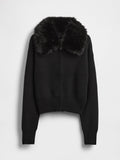 Schwarze, kurze Strickjacke mit gerippter Struktur, ausgestattet mit einem Kunstpelzkragen und einem Frontreißverschluss. Lange Ärmel mit enganliegenden Bündchen.