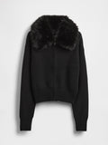 Schwarze, kurze Strickjacke mit gerippter Struktur, ausgestattet mit einem Kunstpelzkragen und einem Frontreißverschluss. Lange Ärmel mit enganliegenden Bündchen.