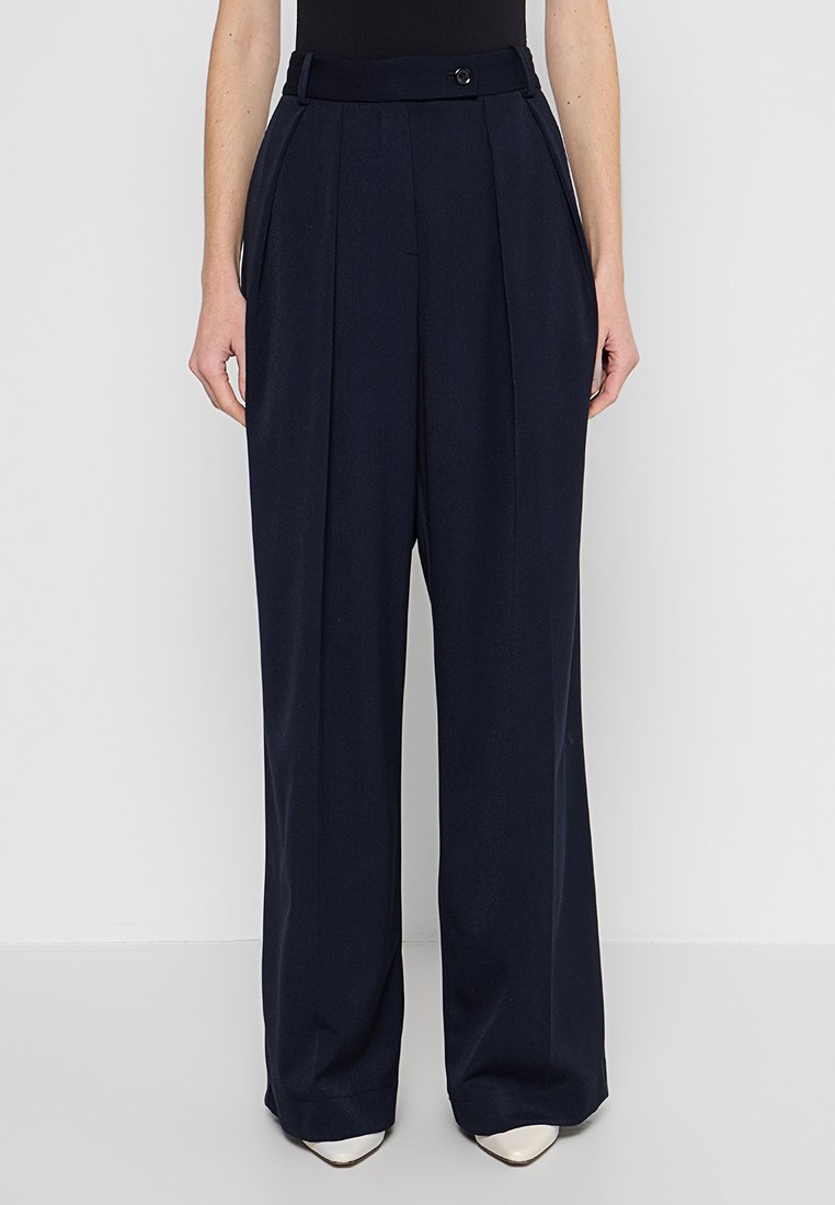 Marineblaue weit geschnittene Hosen mit vorderen Falten, taillierter Passform, hoher Taille und verdecktem Knopfverschluss. Glatte Textur, keine sichtbaren Muster.