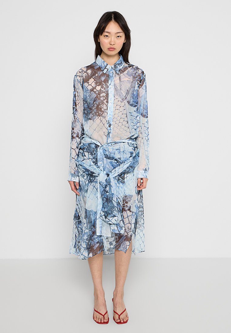 Transparente, langärmlige Hemdkleid in Blau und Weiß mit Schlangendruckmuster; tailliert mit einem Bindegürtel, kombiniert mit roten Sandalen mit Riemchen.