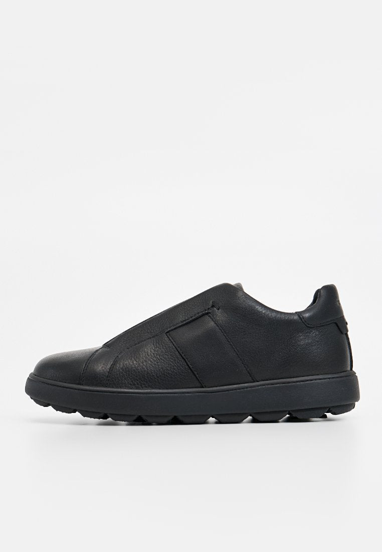 Schwarze Slipper aus strukturiertem Leder mit glatter Oberfläche, ausgestattet mit einer Gummisohle und elastischen Seiteneinsätzen für Flexibilität.
