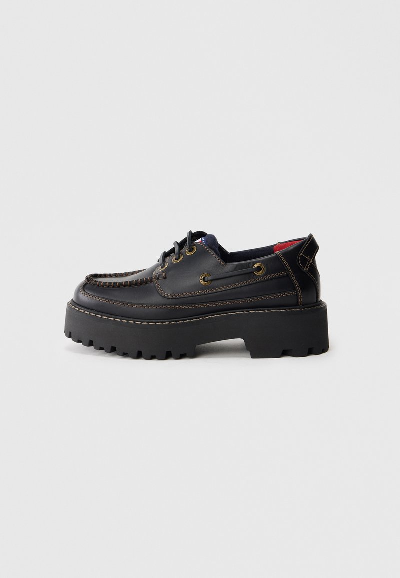 Schwarze Lederschuhe mit abgerundetem Design, dickem schwarzen Plateausohle, dekorativer Stickerei und Messingösen für die Schnürsenkel.