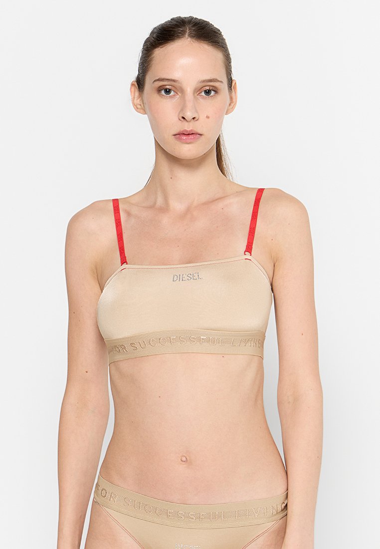 Beige Bralette mit roten Trägern, glatte Textur, mit "DIESEL"-Logo und gemusterter Band, die am unteren Rand "FÜR EINEN ERFOLGREICHEN LEBENSSTIL" liest.