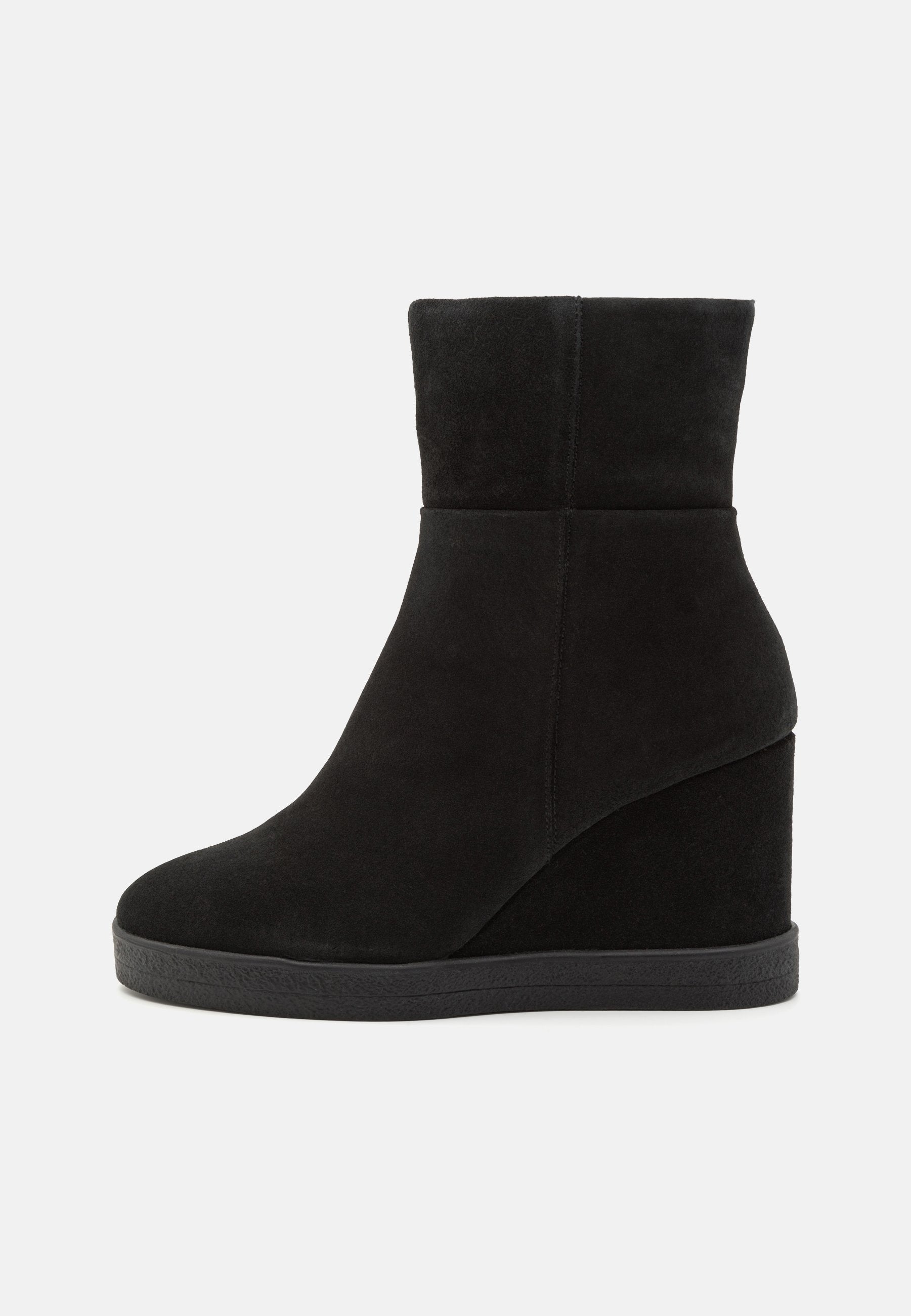Schwarze Wildleder-Wedge-Stiefelette mit runder Zehenpartie und mittelhohem Plattformsohle, nahtloses Oberdesign, seitlich auf weißem Hintergrund betrachtet.