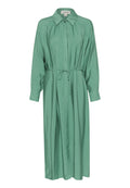 Langes, geknöpftes Kleid aus weichem grünem Stoff, mit einer Knopfleiste an der Vorderseite, einem gebundenen Taillengürtel und langen Ärmeln mit gefütterten Enden. Glatte Textur.